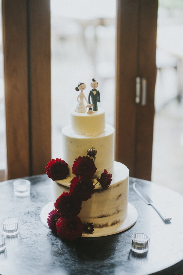 a semi-naked wedding cake with a fondant bride and groom topper and their little dog too