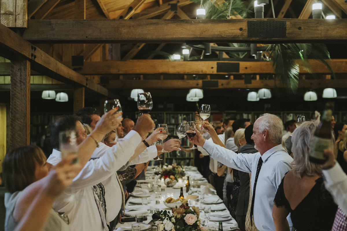 A crowd standing and raising their glasses in a rustic, but elegant barn setting