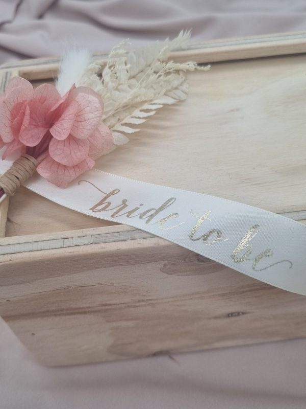 bride to be custom printed ribbon draped on wooden keepsake box with a pink and white dried floral arrangement to decorate