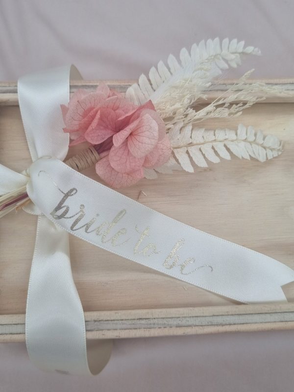 Bride to Be printed in gold foil on white ribbon on keepsake wooden gift box with pink and white dried floral arrangement